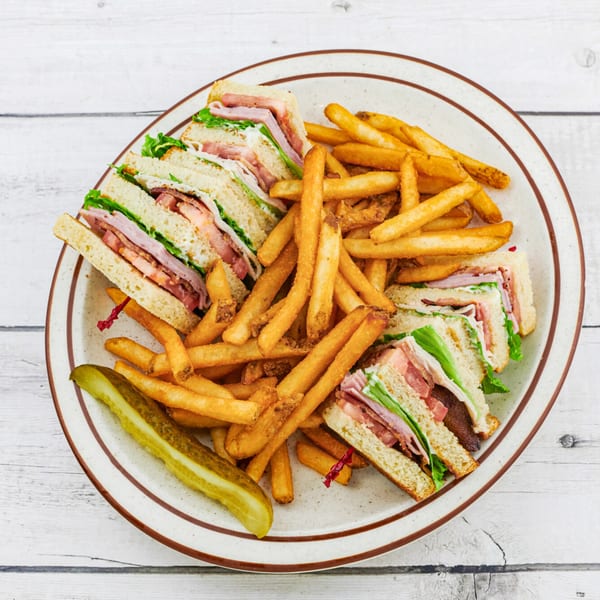 A club sandwich with fries and a pickle spear on a diner plate.