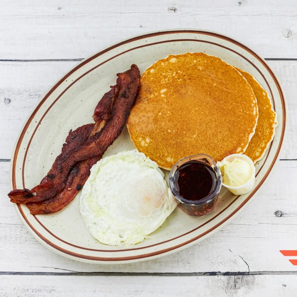 Humpty Dumpty Kitchen's breakfast plate with pancakes, bacon, fried egg, syrup, and butter.